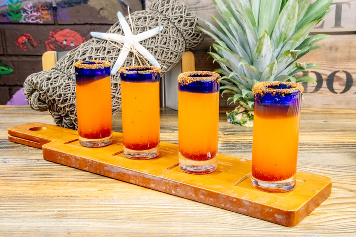 A flight of colorful orange Candy Shots with seasoned rims