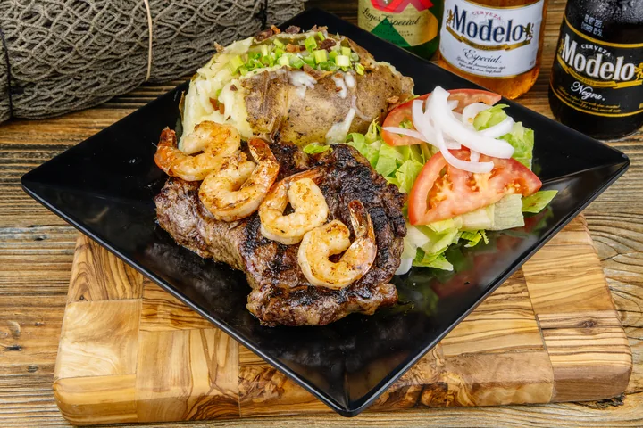Grilled steak topped with shrimp, served with a baked potato and vegetables